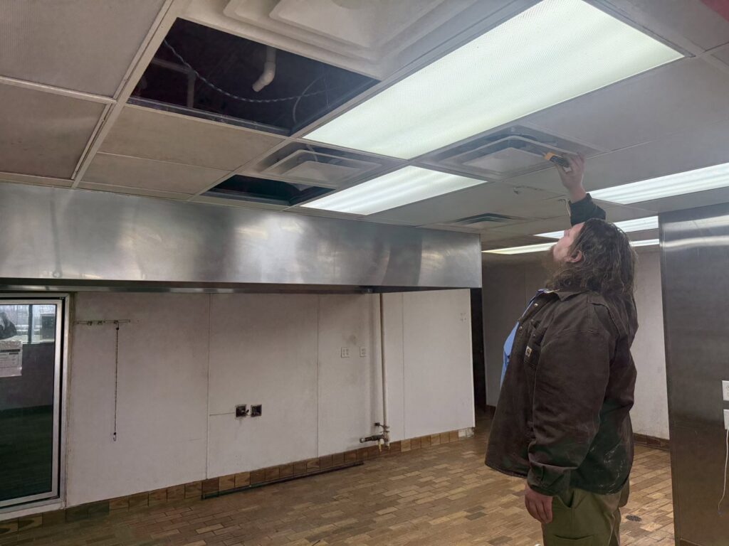 An HVAC technician inspecting ceiling vents and ductwork in a commercial kitchen by Direct Service HVAC & Maintenance in Lewisburg, OH.