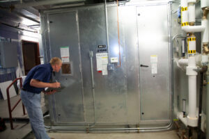 An HVAC technician inspecting a large commercial air handling unit (AHU) for Climate Systems, Inc. in Sioux Falls, SD.