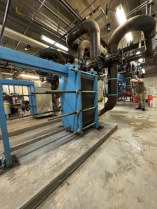 An HVAC technician inspecting a large commercial heat exchanger unit at a job site for APEX HVAC Solutions LLC in Frederick, MD.