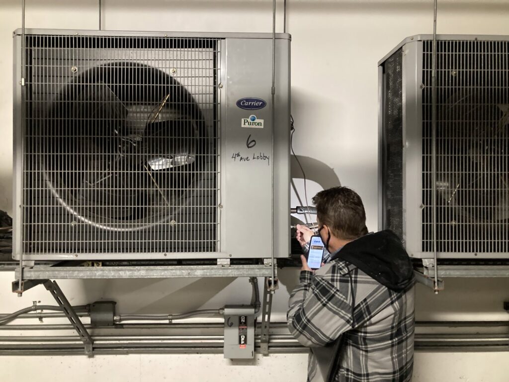 An HVAC technician inspecting a commercial indoor unit and taking a photo for Hurn Mechanical Heating & Cooling in El Cajon, CA.