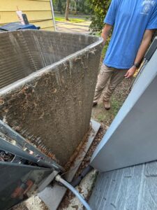 An HVAC technician inspecting a severely dirty outdoor air conditioning coil, highlighting a need for cleaning by Dewees HVAC in Conway, AR.