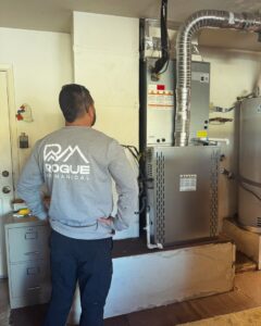 An HVAC technician inspecting a furnace and air handler unit for Rogue Mechanical in Las Vegas, NV.