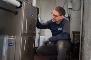 An HVAC technician inspecting a Carrier furnace or air handler for Alan Energy Services in Naperville, IL