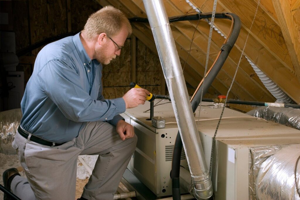 An HVAC technician inspecting a furnace or air handler unit in an attic space for Shook Heating And Cooling in Livonia, MI.