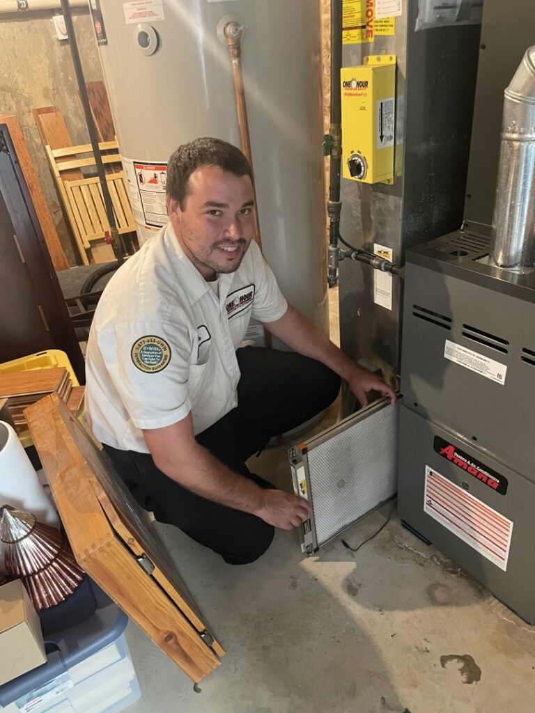 An HVAC technician from One Hour Heating & Air Conditioning of Lancaster, PA, inspecting a furnace air filter in a residential home.