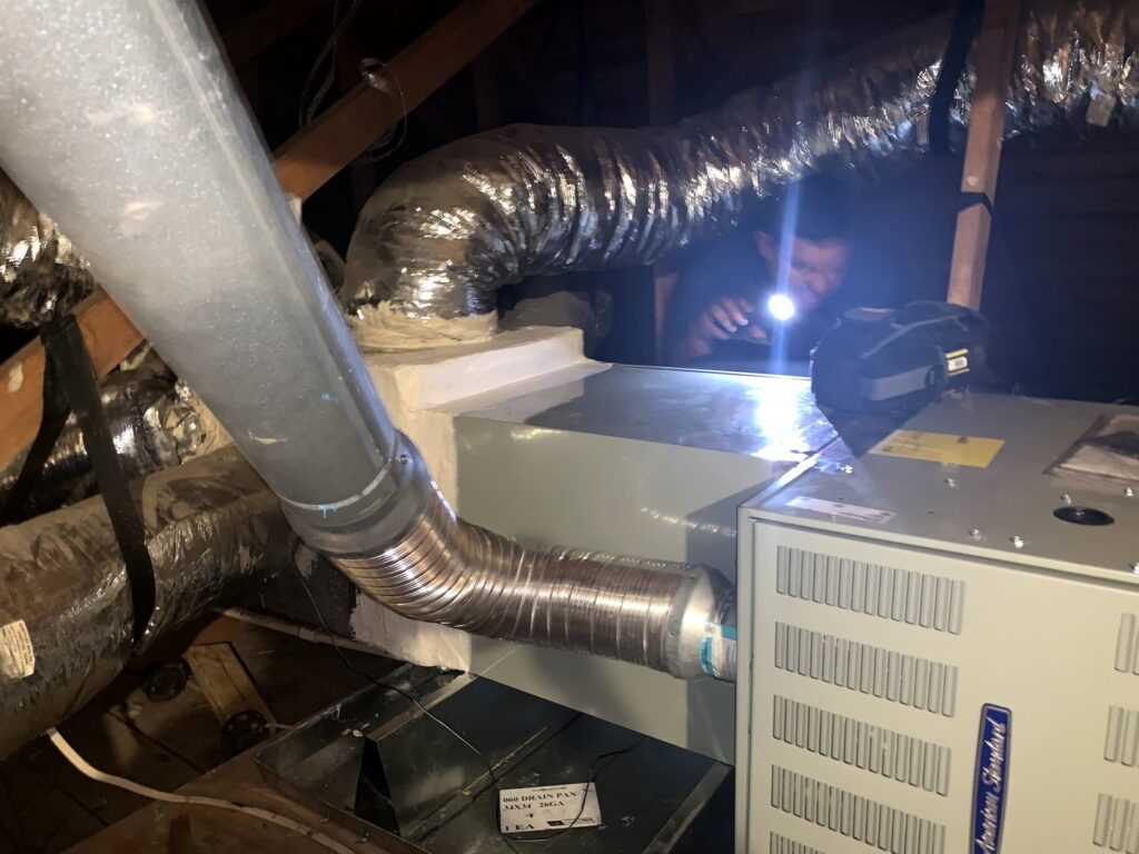 An HVAC technician using a flashlight to inspect an indoor HVAC unit in an attic for Airtegrity Comfort Solutions in San Antonio, TX