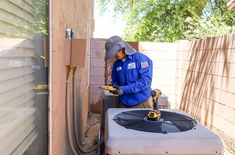 An HVAC technician inspecting an outdoor AC unit with a diagnostic tool for A/C Valley, LLC in Tempe, AZ.