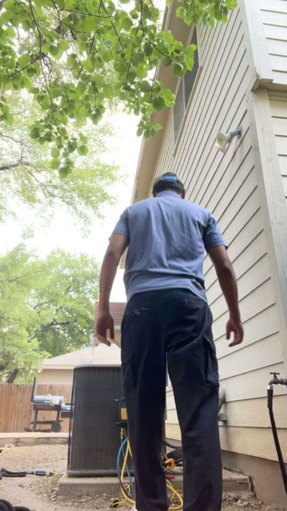 An HVAC technician inspecting an outdoor AC unit with tools on the ground for Airtegrity Comfort Solutions in San Antonio, TX