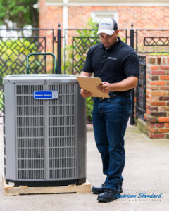 An HVAC technician in uniform inspecting an American Standard outdoor air conditioning unit for VP Supply Corporation in Rochester, NY.
