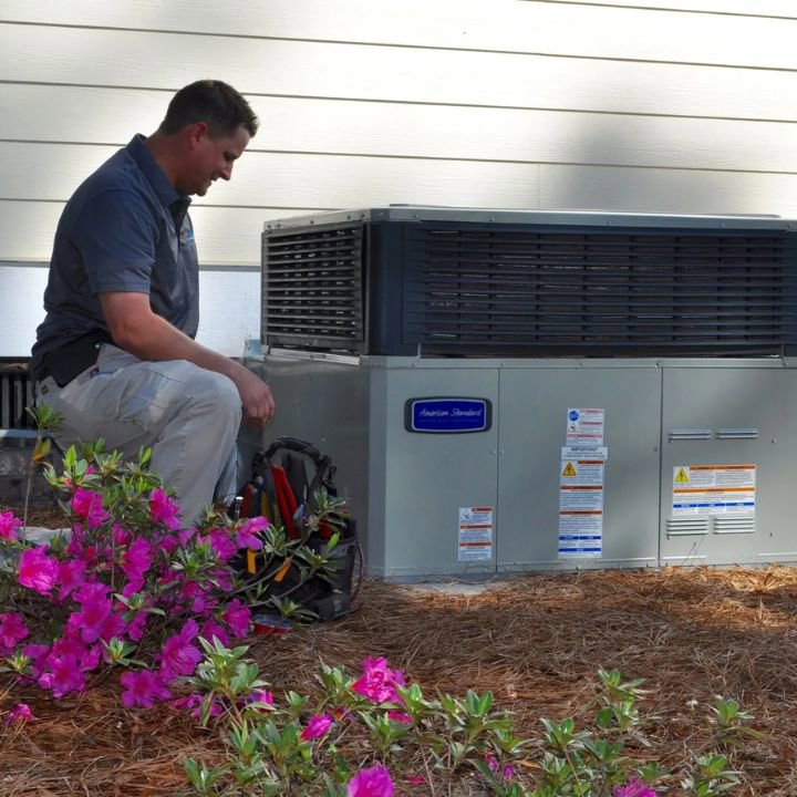 An HVAC technician inspecting an outdoor heating and air conditioning unit for Foust Heating & Air Conditioning in Fayetteville, NC.