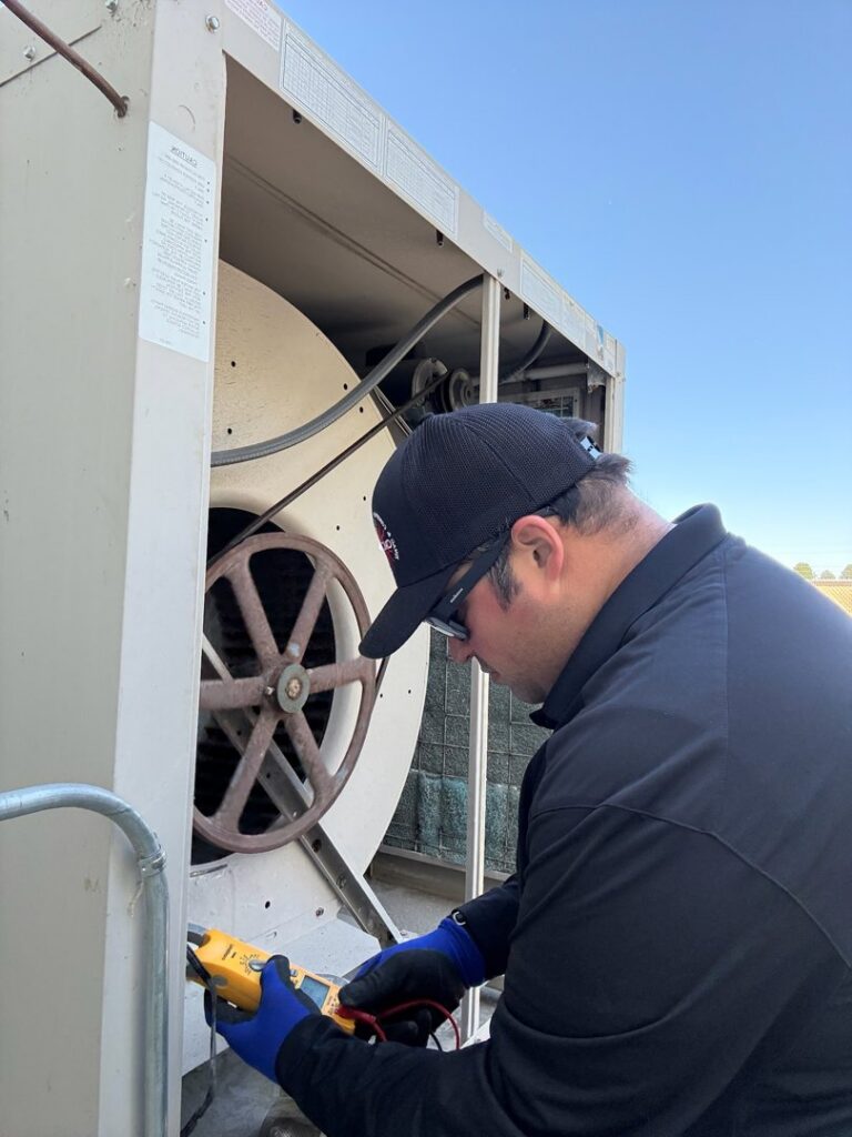 An HVAC technician inspecting the fan and internal components of a large unit for CMC Mechanical, LLC in Caldwell, ID.