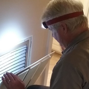 An HVAC technician wearing a headlamp inspects a vent or attic access point for Trusty Air Conditioning in New Orleans, LA.