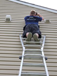 HVAC technician on a ladder inspecting or working on exterior vents on a residential building for Duct Pros in Martinsburg, WV