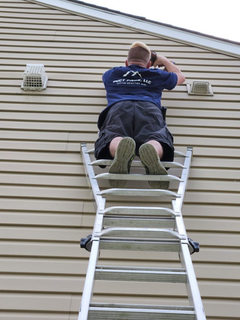 HVAC technician on a ladder inspecting or working on exterior vents on a residential building for Duct Pros in Martinsburg, WV