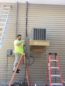 An HVAC technician installing an outdoor AC unit on a wall for Cooler Solutions LLC Heating & Air in Gulfport, MS.
