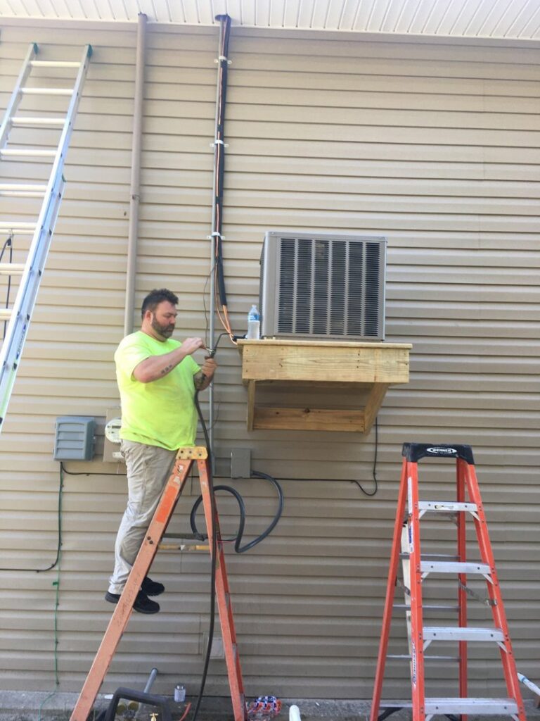 An HVAC technician installing an outdoor AC unit on a wall for Cooler Solutions LLC Heating & Air in Gulfport, MS.
