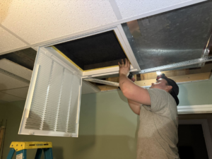 An HVAC technician installing an air filter in a ceiling return vent for Workman Mechanical in Graham, NC.