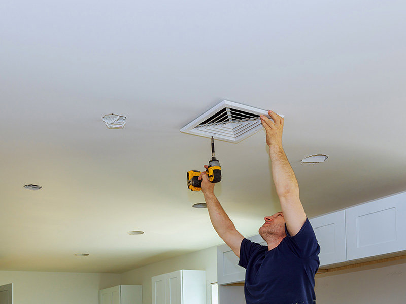 An HVAC technician installing a ceiling vent with a drill for Baker Heating & Cooling in Dayton, OH.
