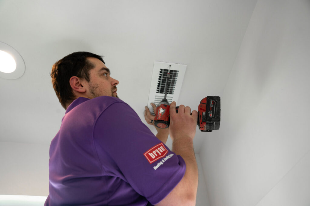An HVAC technician from CSA HVAC Services installing a ceiling air vent with a drill in Orem, UT.