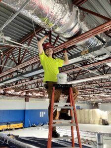 An HVAC technician installing commercial ductwork on a ladder for Blue Fox Heating & Cooling in Lebanon, IN.