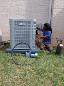 An HVAC technician installing or servicing an outdoor condenser unit with a vacuum pump for Sterling Service of Florida Inc in Tallahassee, FL.