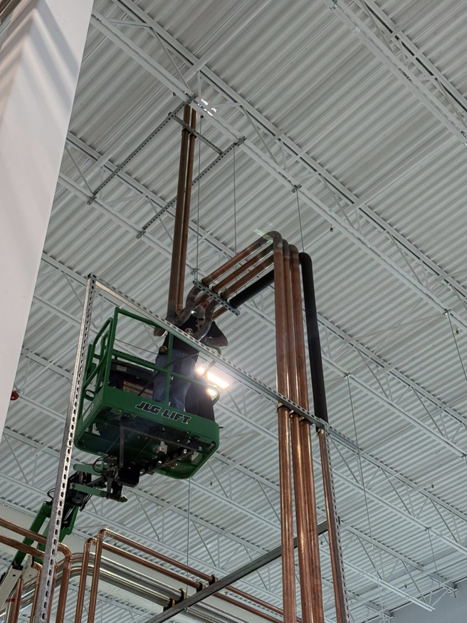 An HVAC technician in a JLG lift installing copper piping in a commercial building for KCC Mechanical, LLC in Sandy, UT.