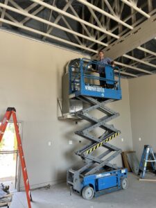An HVAC technician on a scissor lift installing ductwork in a commercial building for Advanced Comfort A/C & Heating in Phoenix, AZ.