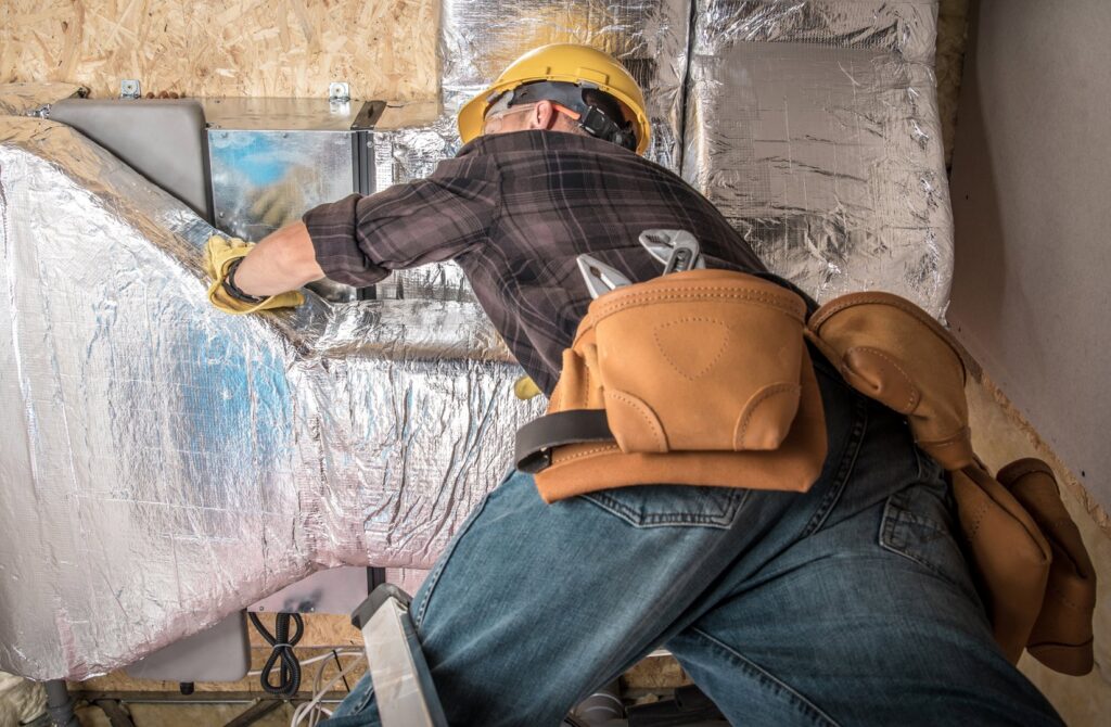 An HVAC technician installing or repairing ductwork in a building for Air Fix in Fayetteville, AR.