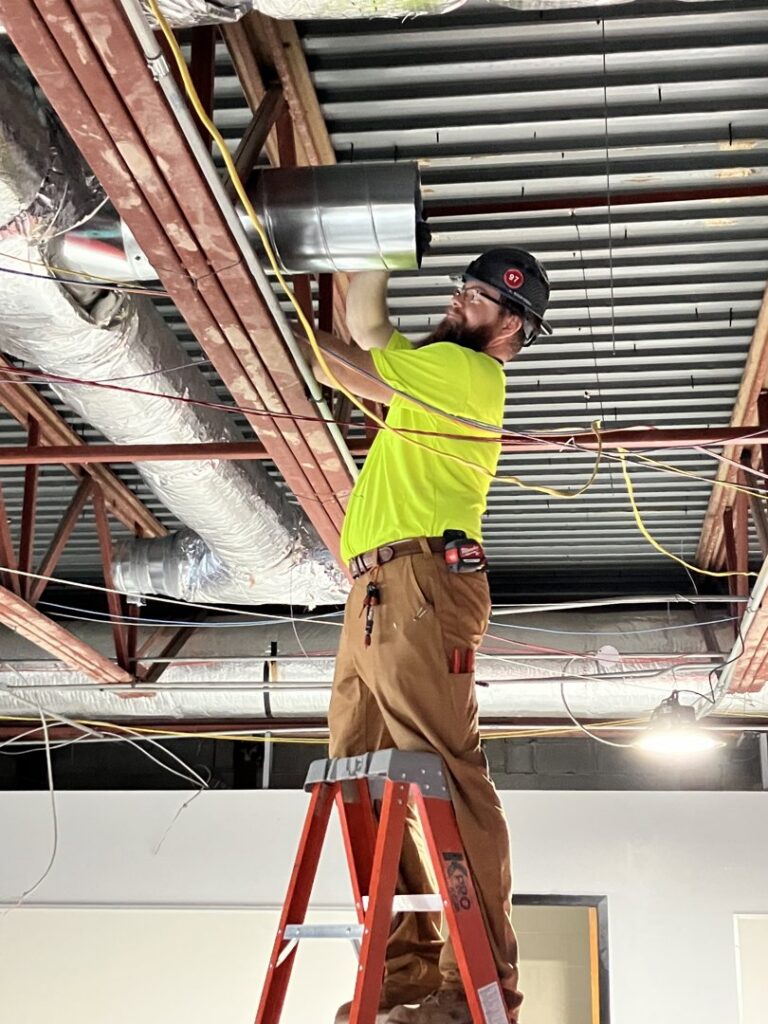 An HVAC technician installing ductwork in a commercial building for Blue Fox Heating & Cooling in Lebanon, IN.