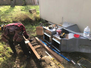 An HVAC technician from Columbia Heating & Air Conditioning installing or repairing ductwork outdoors in Kent, WA.