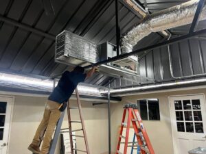An HVAC technician installing ductwork and an indoor unit for Genesis - Heating and Air Conditioning Specialist in SUNNYSIDE, NY