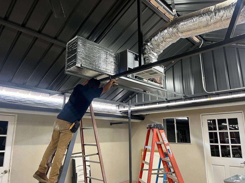 An HVAC technician installing ductwork and an indoor unit for Genesis - Heating and Air Conditioning Specialist in SUNNYSIDE, NY
