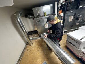 An HVAC technician installing new ductwork for a heating system at HeatSource Mechanical in Wasilla, AK.