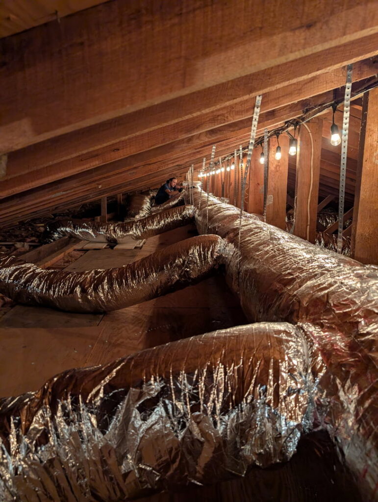 An Air Specialty Heating & Air Conditioning technician installing or repairing ductwork in an attic in Norfolk, VA.