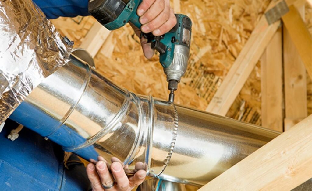 An HVAC technician installing metal ductwork with a drill during a job by J & J Heating and Cooling, Inc. in Lancaster, PA.