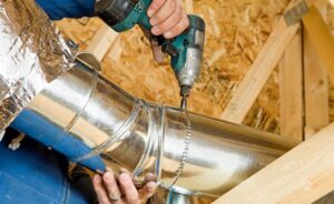 An HVAC technician installing metal ductwork with a drill during a job by J & J Heating and Cooling, Inc. in Lancaster, PA.
