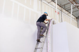 An HVAC technician on a ladder installing ductwork during a service call by Surfside Heating & Cooling in Cape Coral, FL.