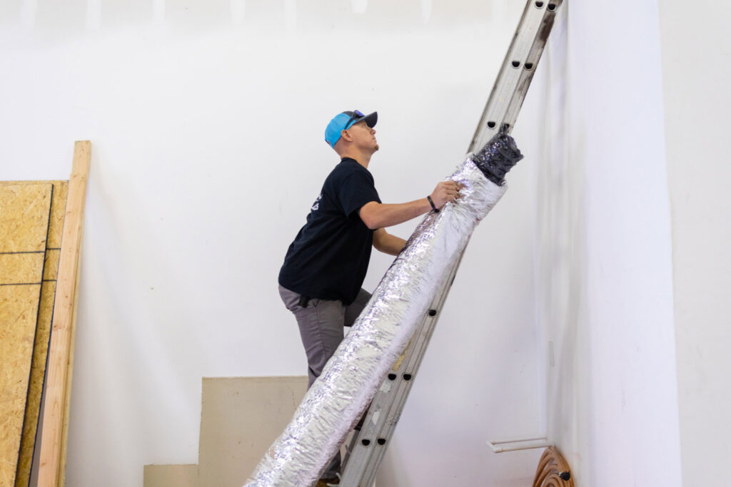 An HVAC technician carrying ductwork up a ladder for installation by Surfside Heating & Cooling in Cape Coral, FL.