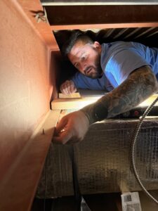 An HVAC technician installing or repairing ductwork in a tight space for Wright Way Air in Streamwood, IL