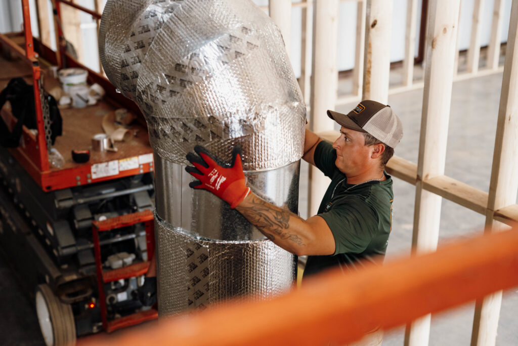 An HVAC technician installing insulated ductwork in a building under construction for Wingman Heating + Cooling in Auburn, AL.