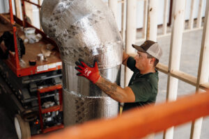 An HVAC technician installing insulated ductwork in a building under construction for Wingman Heating + Cooling in Auburn, AL.