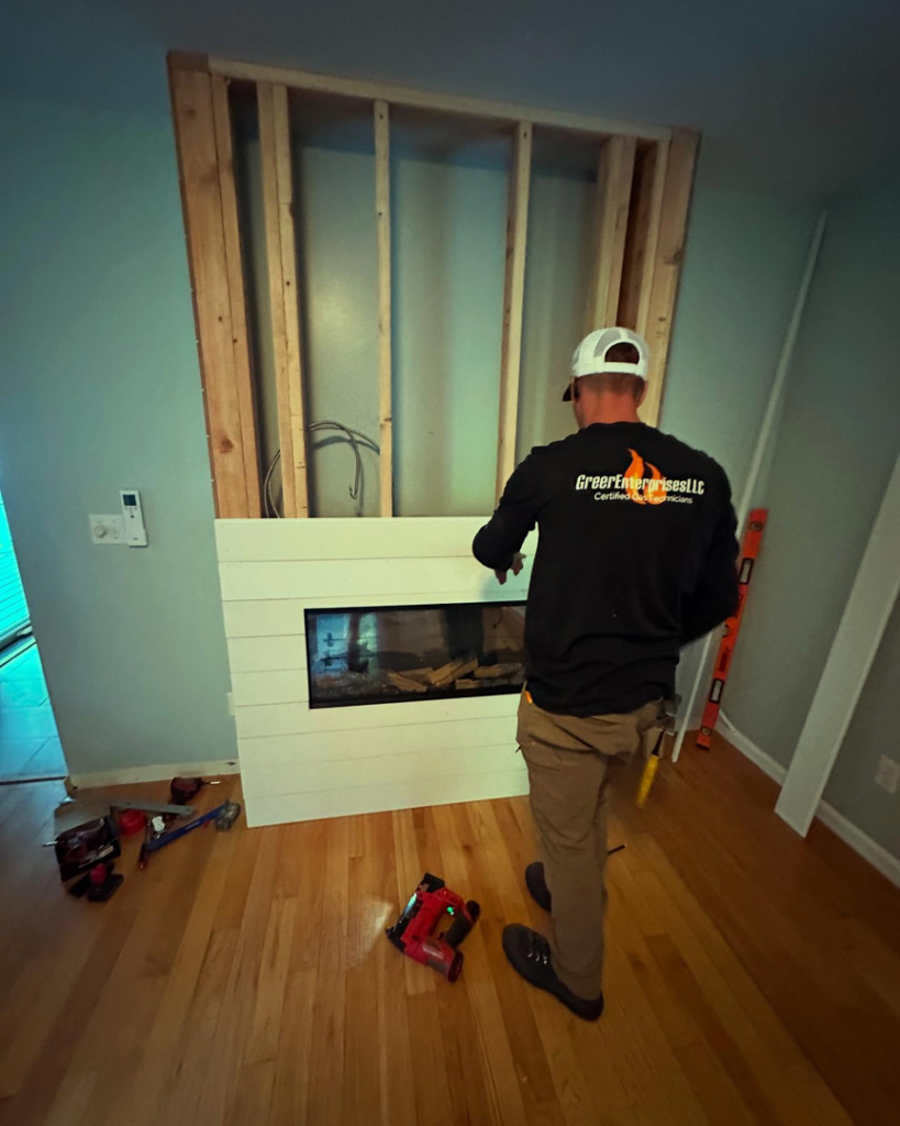 An HVAC technician from Greer Enterprises installing an electric fireplace in a home in Raymond, NH.