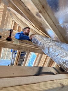 An HVAC technician installing insulated flexible ductwork in a new construction ceiling for Dewees HVAC in Conway, AR.