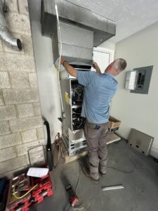 An HVAC technician installing or repairing furnace ductwork in a residential basement for Radiant Heating & Cooling in Fishers, IN.