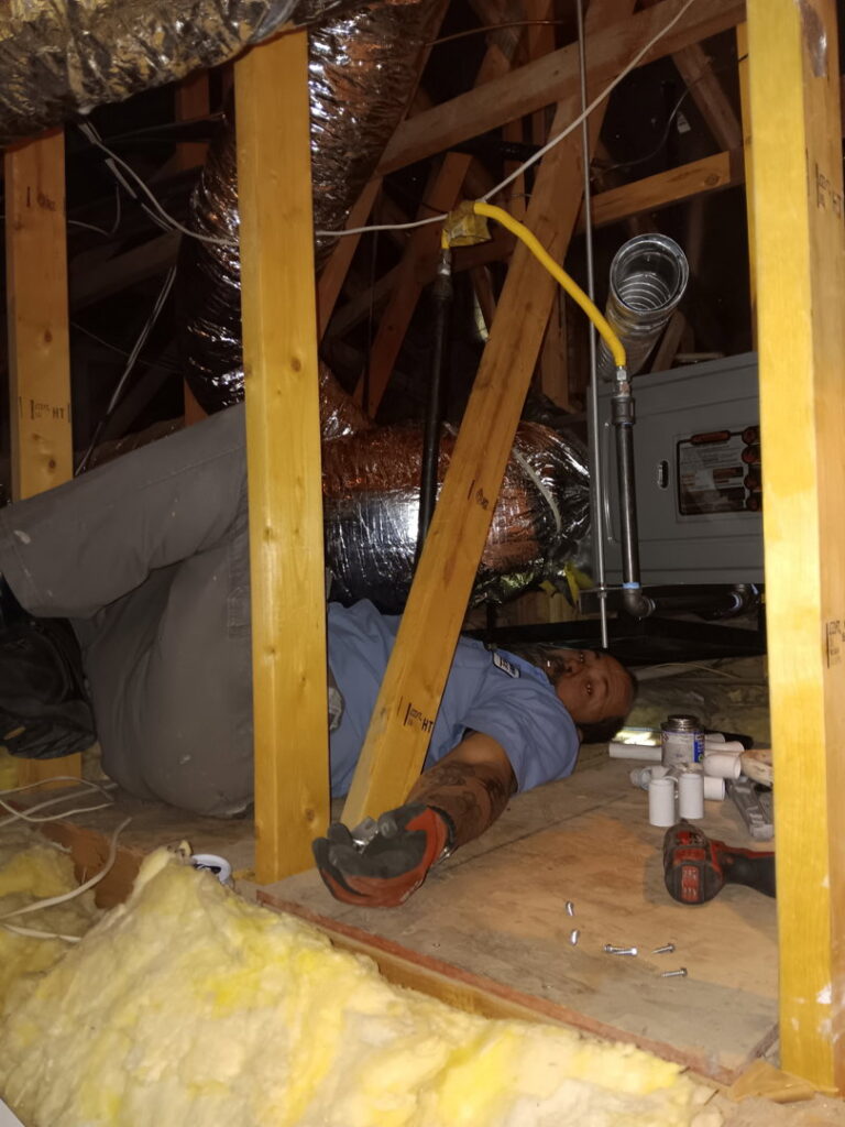 An HVAC technician installing a gas line and working on ductwork in an attic for Bishop Air Service in Henderson, NV.