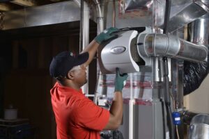 An HVAC technician installing an Aprilaire whole-home humidifier for Isaac Heating & Air Conditioning in Rochester, NY.