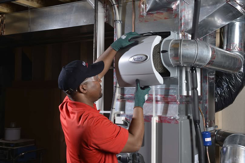 An HVAC technician installing an Aprilaire whole-home humidifier for Isaac Heating & Air Conditioning in Rochester, NY.
