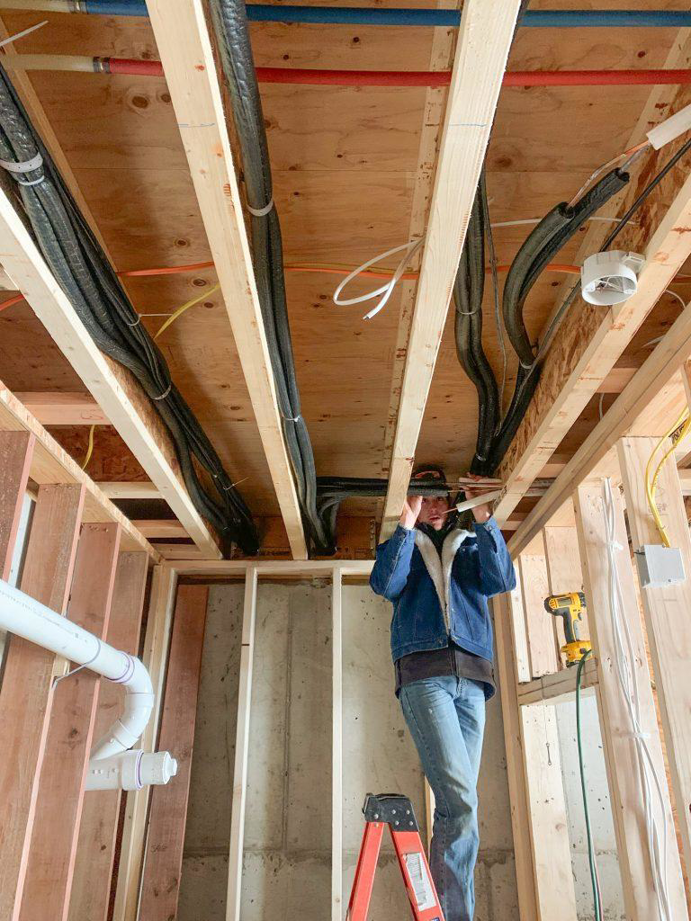 An HVAC technician installing insulated lines and ductwork in a new construction ceiling for Bishop Air Service in Henderson, NV.