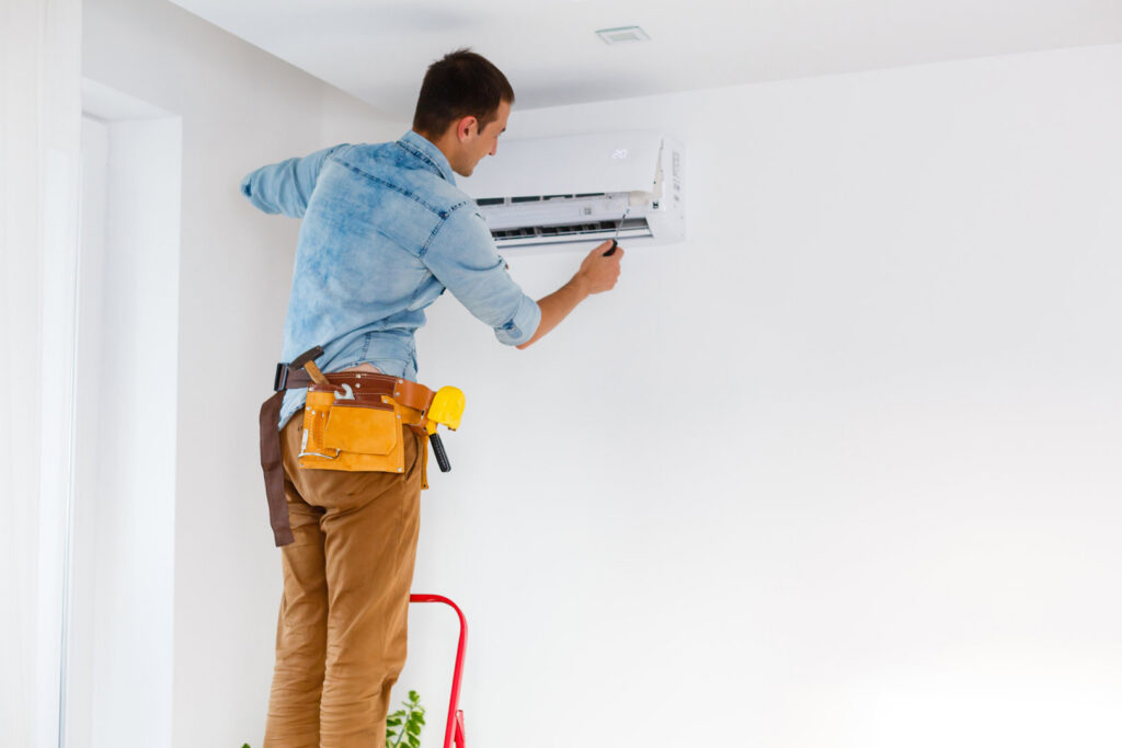 An HVAC technician on a ladder installing an indoor mini-split air conditioning unit for Reed's Heating & Cooling in Toms River, NJ.