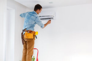 An HVAC technician on a ladder installing an indoor mini-split air conditioning unit for Reed's Heating & Cooling in Toms River, NJ.